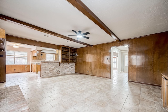 unfurnished living room featuring ceiling fan, light tile patterned floors, wood walls, visible vents, and beamed ceiling