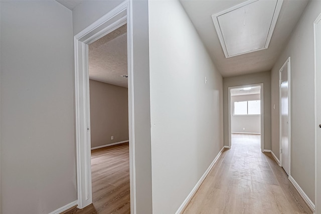 corridor featuring light wood finished floors, attic access, and baseboards