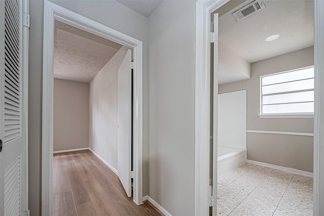 corridor with baseboards, visible vents, and a textured ceiling