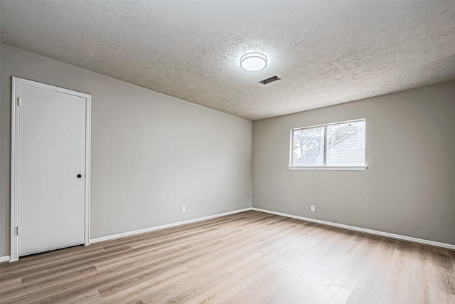 unfurnished room with a textured ceiling, wood finished floors, visible vents, and baseboards