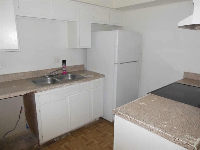 kitchen featuring white cabinets, freestanding refrigerator, range hood, light countertops, and a sink