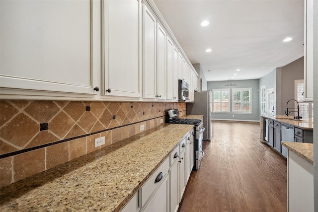 kitchen with white cabinets, dark wood finished floors, decorative backsplash, stainless steel appliances, and a sink