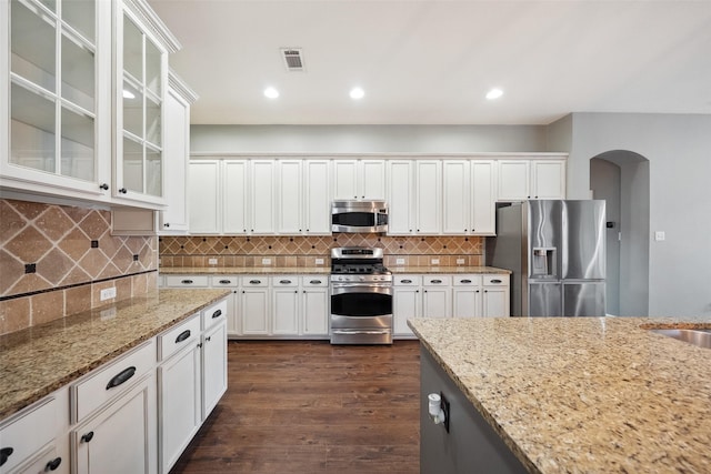 kitchen featuring visible vents, arched walkways, decorative backsplash, appliances with stainless steel finishes, and light stone countertops