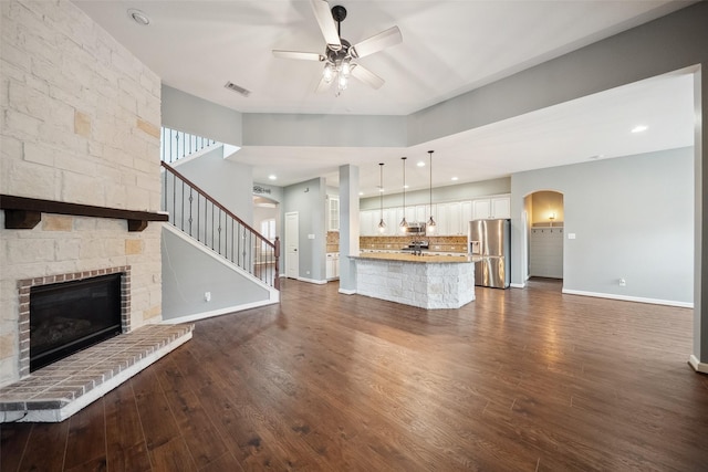 unfurnished living room featuring dark wood-type flooring, visible vents, a fireplace, and a ceiling fan