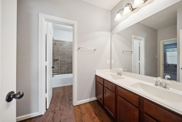 full bathroom with double vanity, a sink, baseboards, and wood finished floors