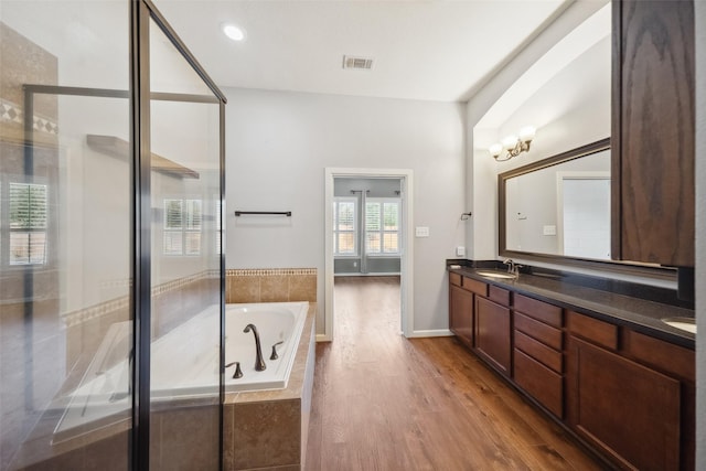 full bath featuring double vanity, wood finished floors, a garden tub, a shower stall, and a sink