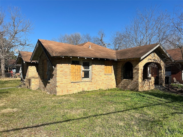 view of side of property featuring a yard, a shingled roof, and brick siding