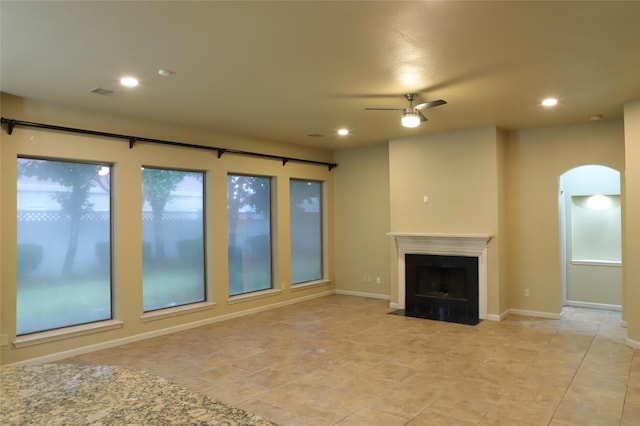 unfurnished living room with ceiling fan, arched walkways, a fireplace with flush hearth, and recessed lighting