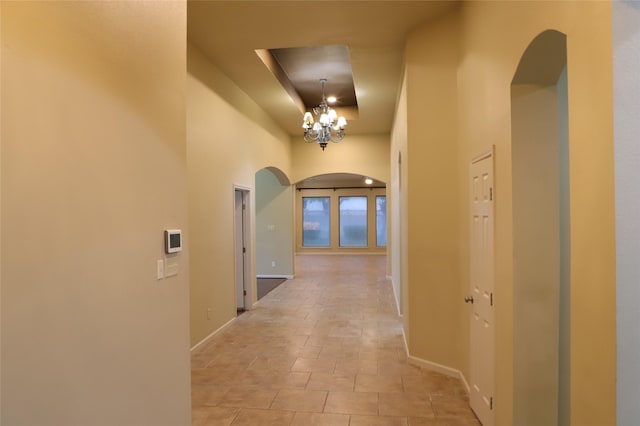 corridor featuring arched walkways, light tile patterned floors, baseboards, and an inviting chandelier