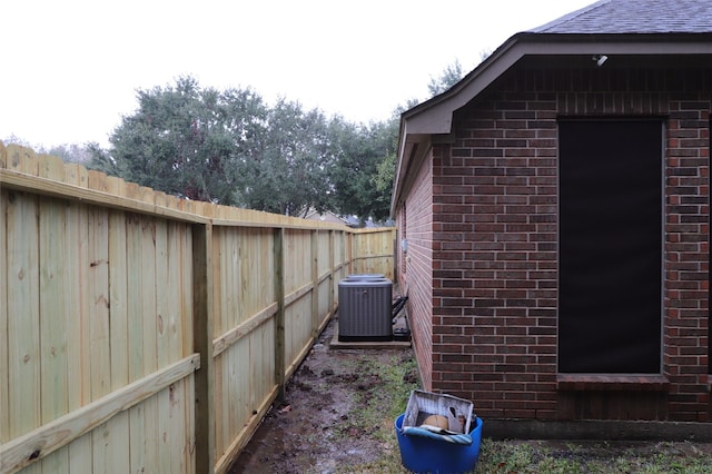 view of property exterior featuring cooling unit, a fenced backyard, brick siding, and roof with shingles