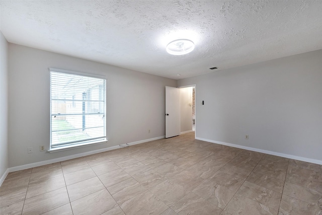 spare room with visible vents, a textured ceiling, and baseboards