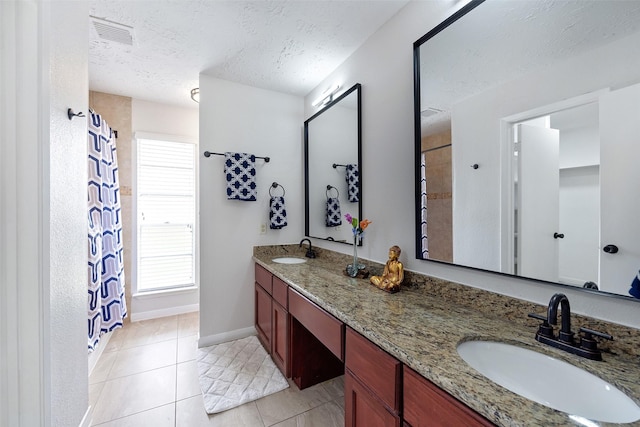 bathroom with a textured ceiling, double vanity, a sink, and baseboards