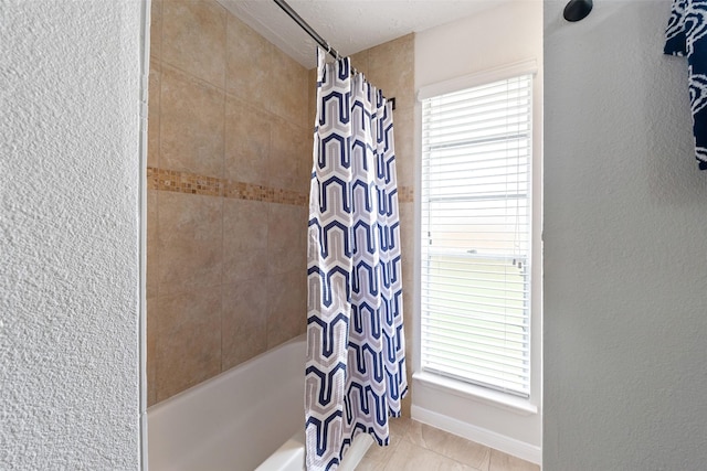 full bathroom featuring shower / bath combination with curtain, a textured wall, baseboards, and tile patterned floors