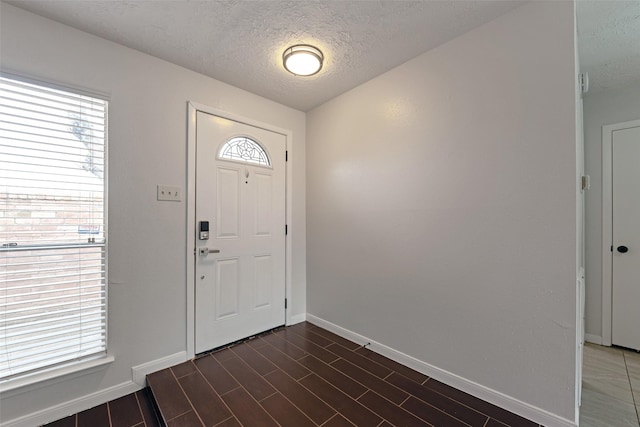 foyer with dark wood-style flooring, a textured ceiling, and baseboards