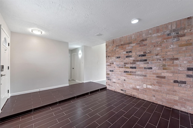 unfurnished room with brick wall, visible vents, a textured ceiling, and baseboards