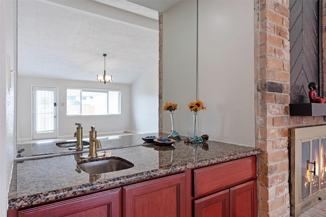 kitchen with lofted ceiling, a brick fireplace, a sink, and dark stone countertops