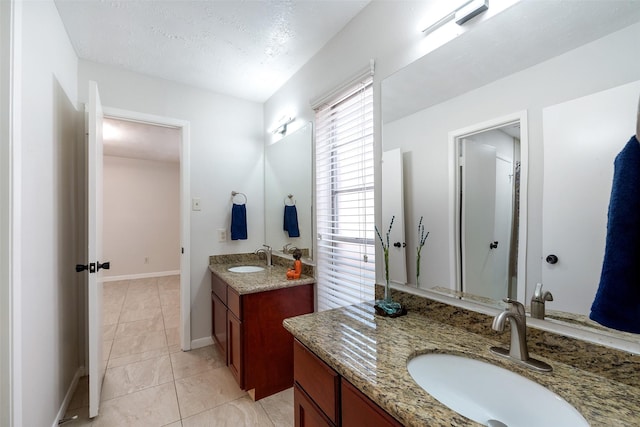 bathroom with a textured ceiling, two vanities, a sink, baseboards, and tile patterned floors