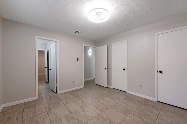 unfurnished bedroom with multiple closets, baseboards, visible vents, and a textured ceiling