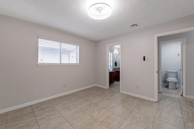 unfurnished bedroom with visible vents, connected bathroom, a textured ceiling, and baseboards