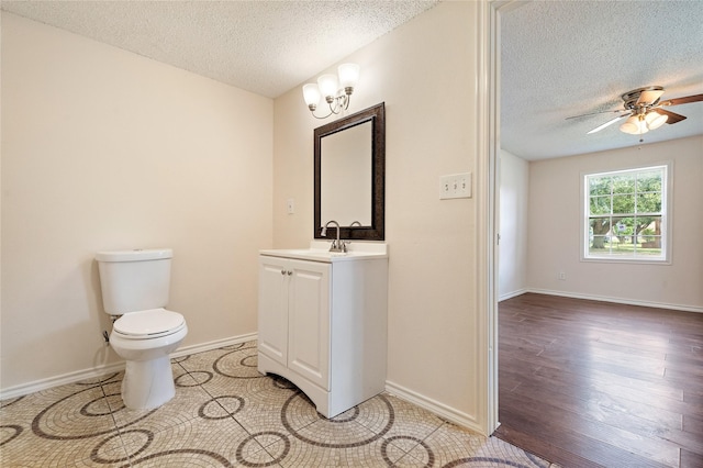 half bath featuring toilet, a ceiling fan, vanity, a textured ceiling, and baseboards