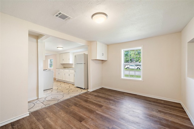 interior space featuring a textured ceiling, wood finished floors, visible vents, baseboards, and washer / clothes dryer