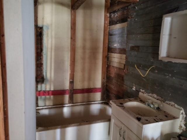 full bathroom with a tub to relax in, wooden walls, and vanity