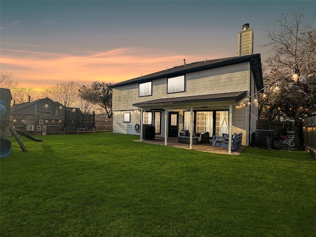 back of property at dusk with a patio area, a fenced backyard, a lawn, and a trampoline