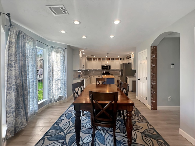 dining area with visible vents, light wood-style flooring, recessed lighting, arched walkways, and baseboards