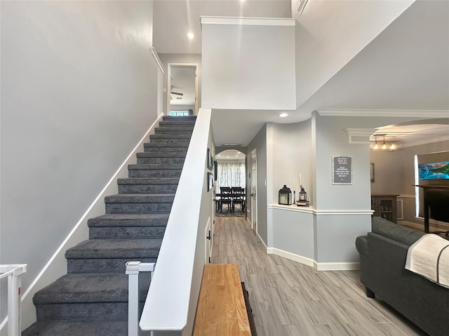 stairs with wood finished floors, baseboards, recessed lighting, arched walkways, and crown molding