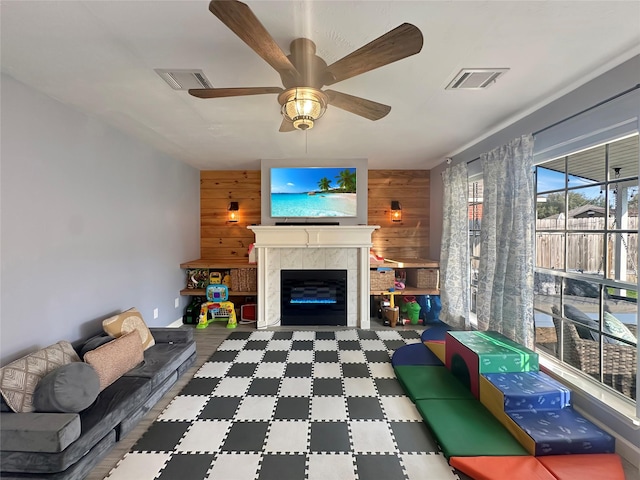 living room featuring ceiling fan, visible vents, wood walls, and a tile fireplace