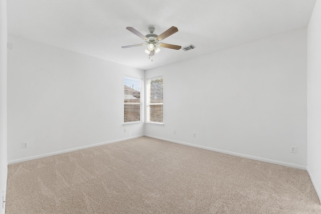 spare room with light carpet, visible vents, a ceiling fan, and baseboards