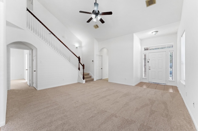 unfurnished living room with light carpet, stairway, arched walkways, and a high ceiling