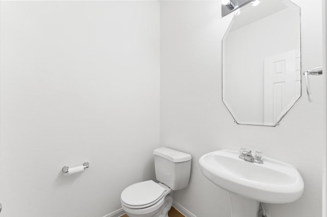 half bath featuring a sink, baseboards, and toilet