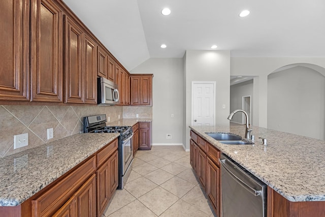 kitchen featuring light tile patterned floors, arched walkways, a sink, appliances with stainless steel finishes, and tasteful backsplash