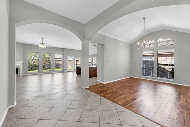 spare room with baseboards, lofted ceiling, ceiling fan with notable chandelier, light wood-style floors, and arched walkways