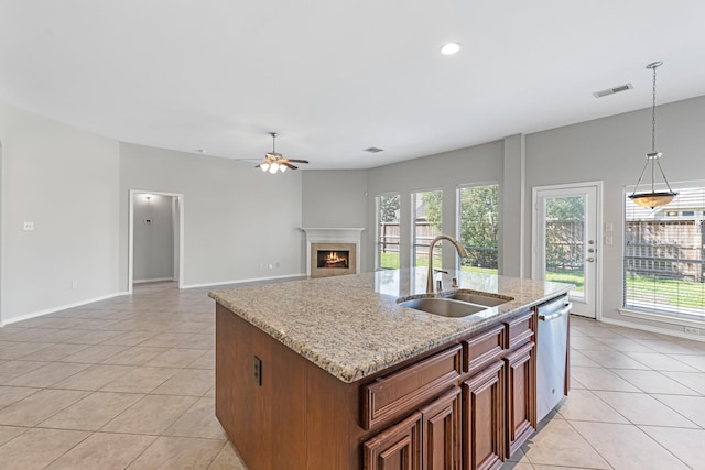 kitchen with a ceiling fan, a sink, stainless steel dishwasher, a warm lit fireplace, and light tile patterned flooring