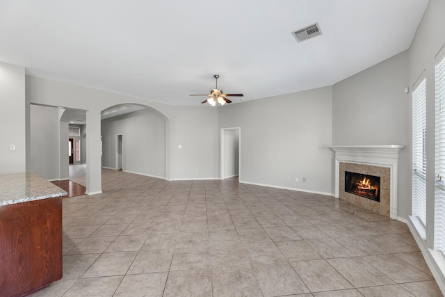 unfurnished living room with visible vents, a fireplace, light tile patterned floors, baseboards, and ceiling fan