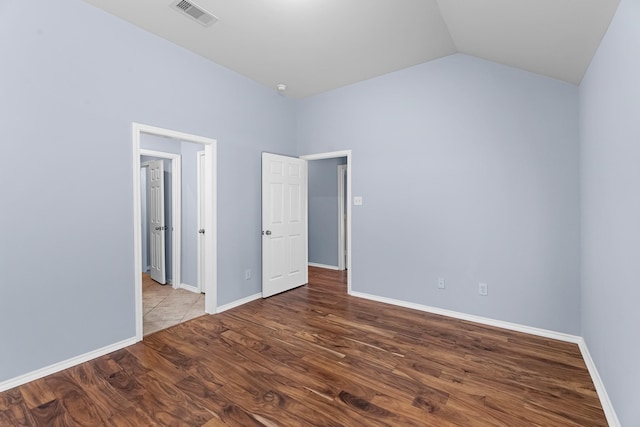 empty room featuring vaulted ceiling, visible vents, baseboards, and wood finished floors