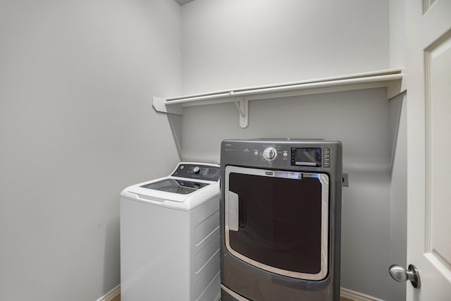 clothes washing area with laundry area, baseboards, and washer and clothes dryer