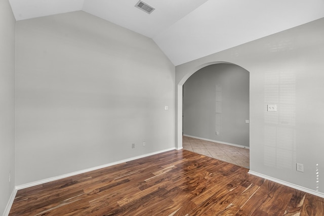 unfurnished room with wood finished floors, baseboards, visible vents, lofted ceiling, and arched walkways