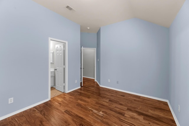 unfurnished bedroom featuring visible vents, ensuite bath, wood finished floors, baseboards, and vaulted ceiling