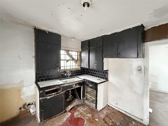 kitchen with light countertops, dark cabinetry, backsplash, and a sink