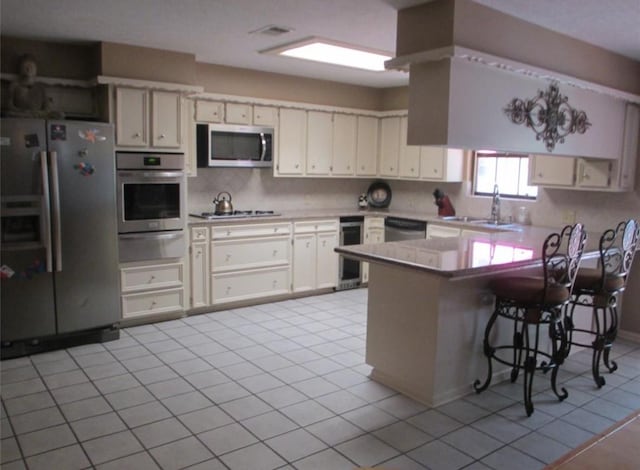 kitchen featuring decorative backsplash, appliances with stainless steel finishes, a breakfast bar, a peninsula, and a sink