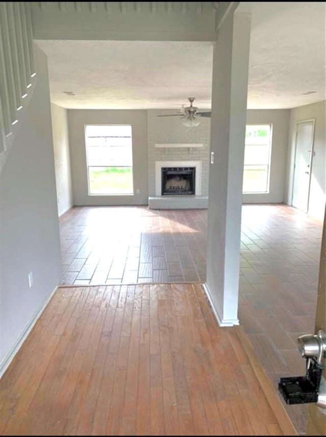 unfurnished living room with a healthy amount of sunlight, a ceiling fan, a fireplace with raised hearth, and wood finished floors