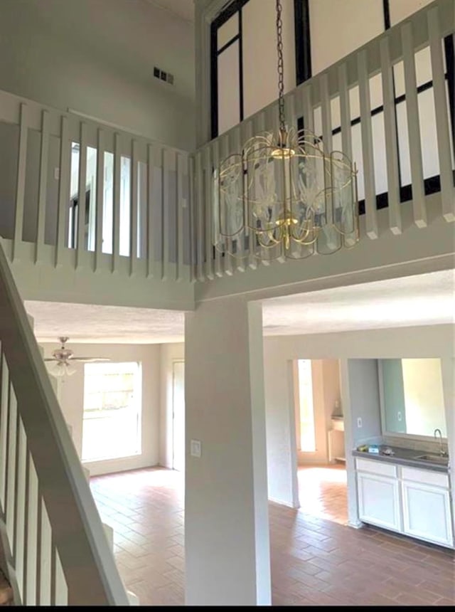 stairs with brick floor, visible vents, a towering ceiling, and ceiling fan with notable chandelier