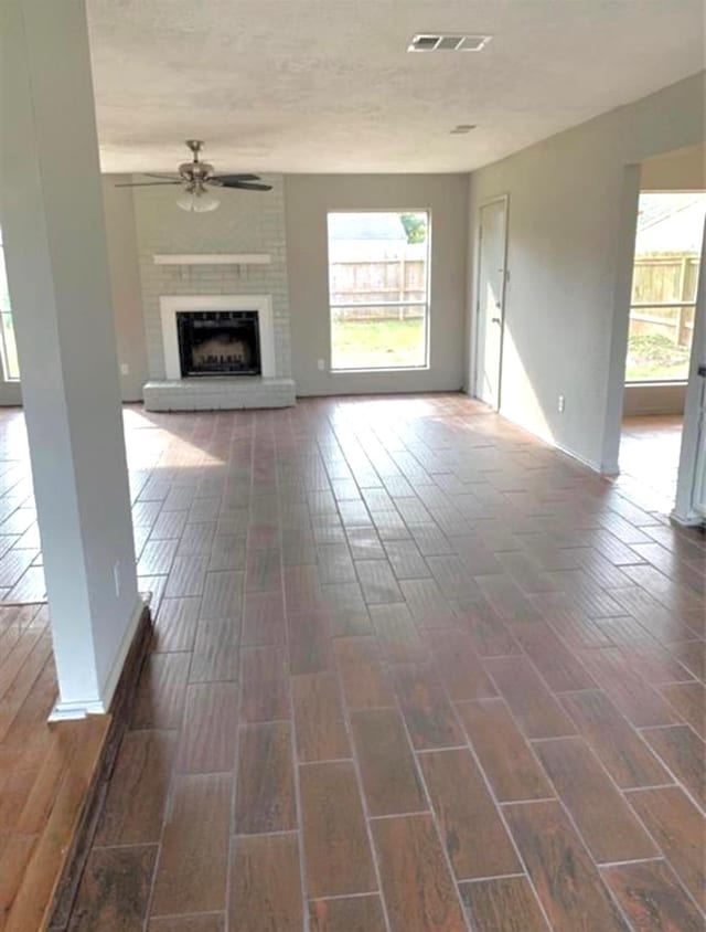 unfurnished living room with visible vents, ceiling fan, a textured ceiling, wood finish floors, and a brick fireplace