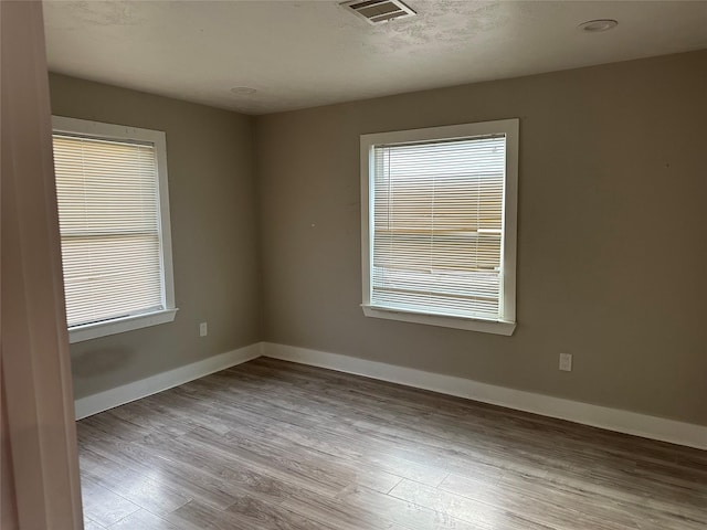 unfurnished room with a textured ceiling, wood finished floors, visible vents, and baseboards