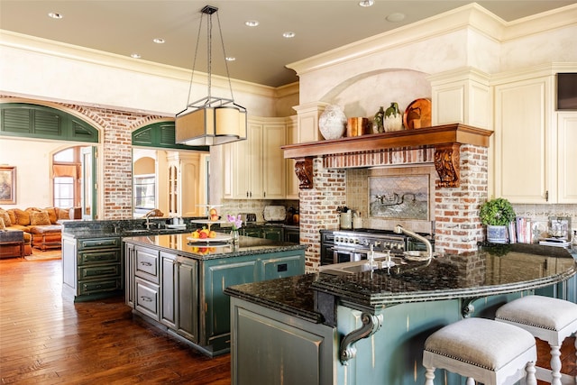 kitchen with cream cabinetry, dark wood finished floors, an island with sink, and dark stone countertops