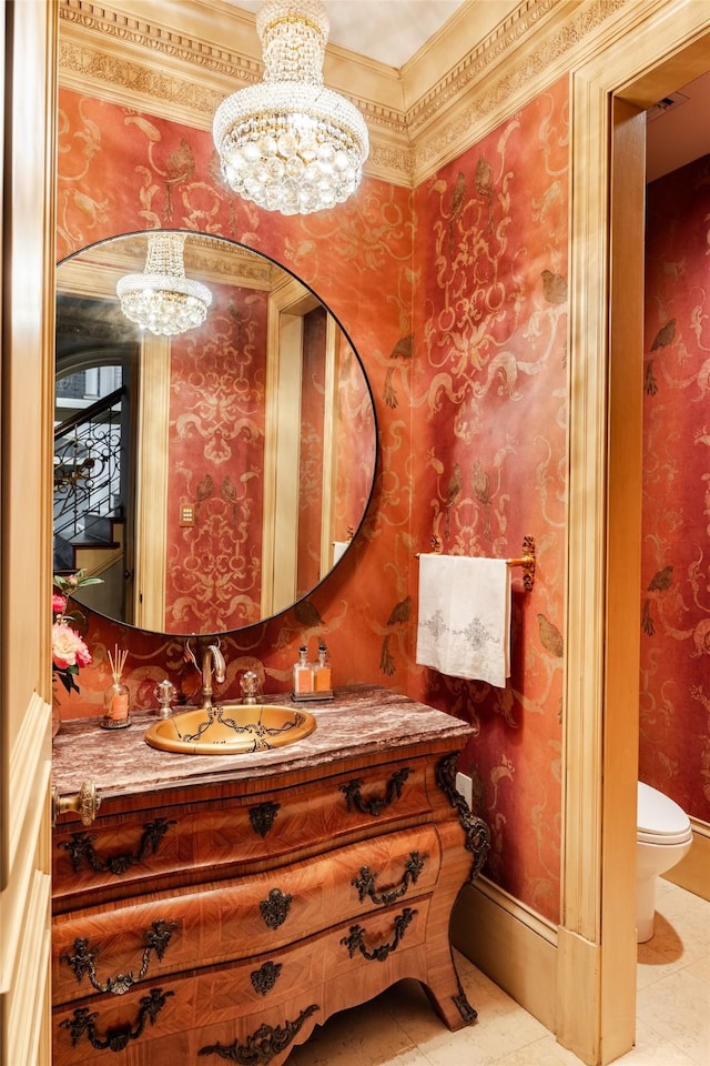 half bathroom with a notable chandelier, toilet, vanity, baseboards, and wallpapered walls