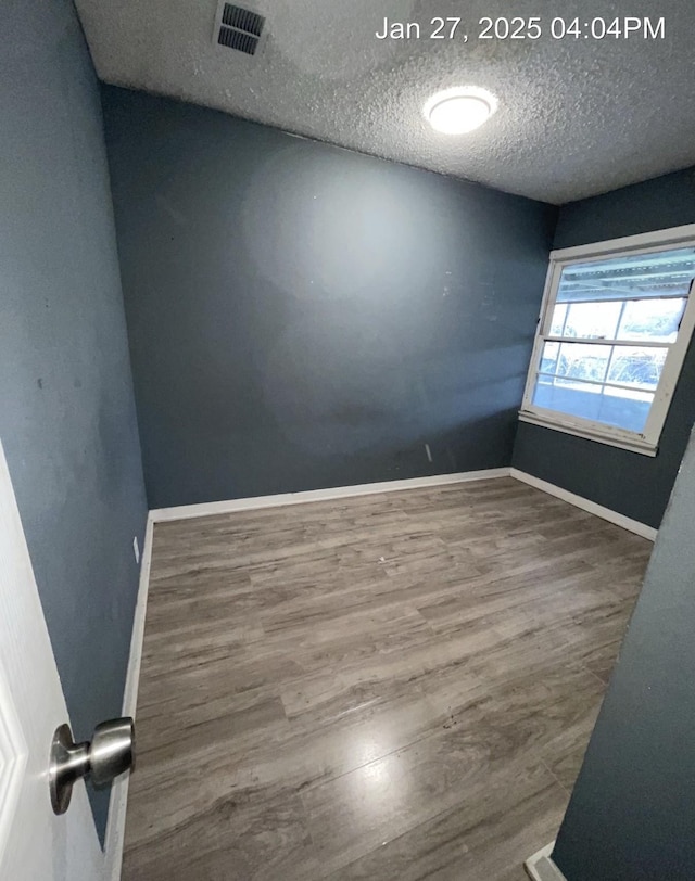 spare room with a textured ceiling, wood finished floors, visible vents, and baseboards